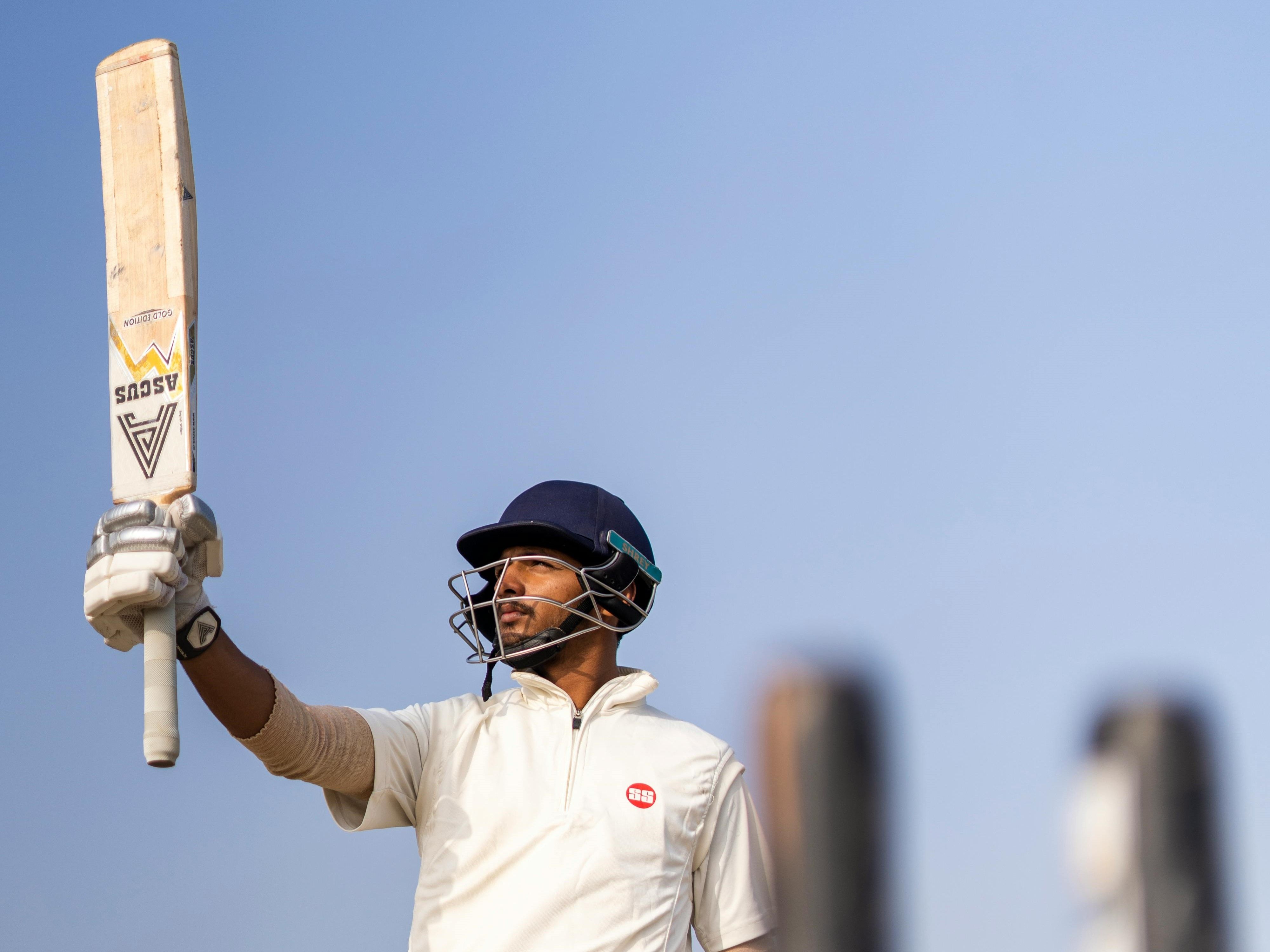 Indian cricket player holding bat proudly in the air